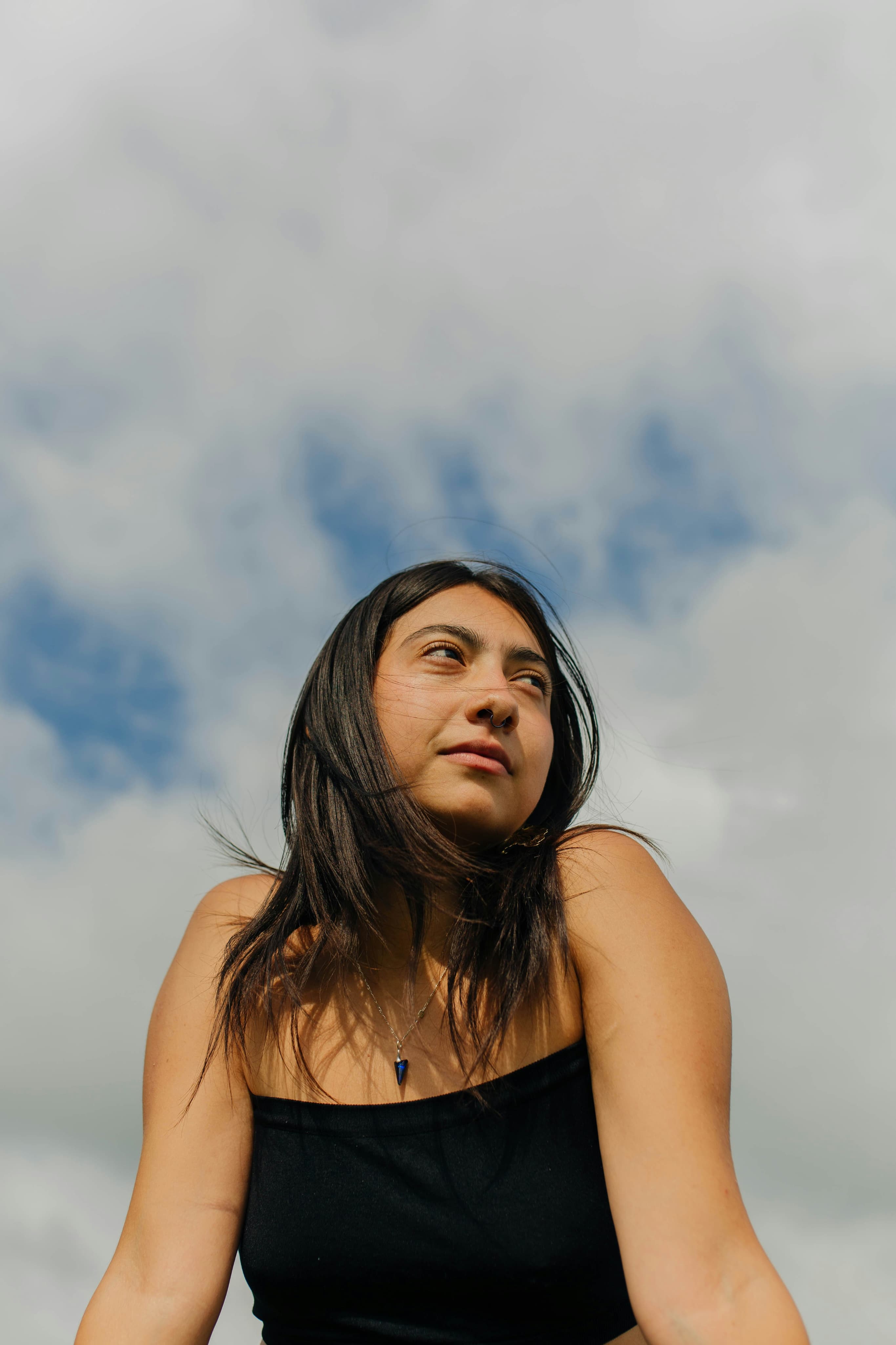 A person in a black top with a blue pendant against a cloudy sky background.