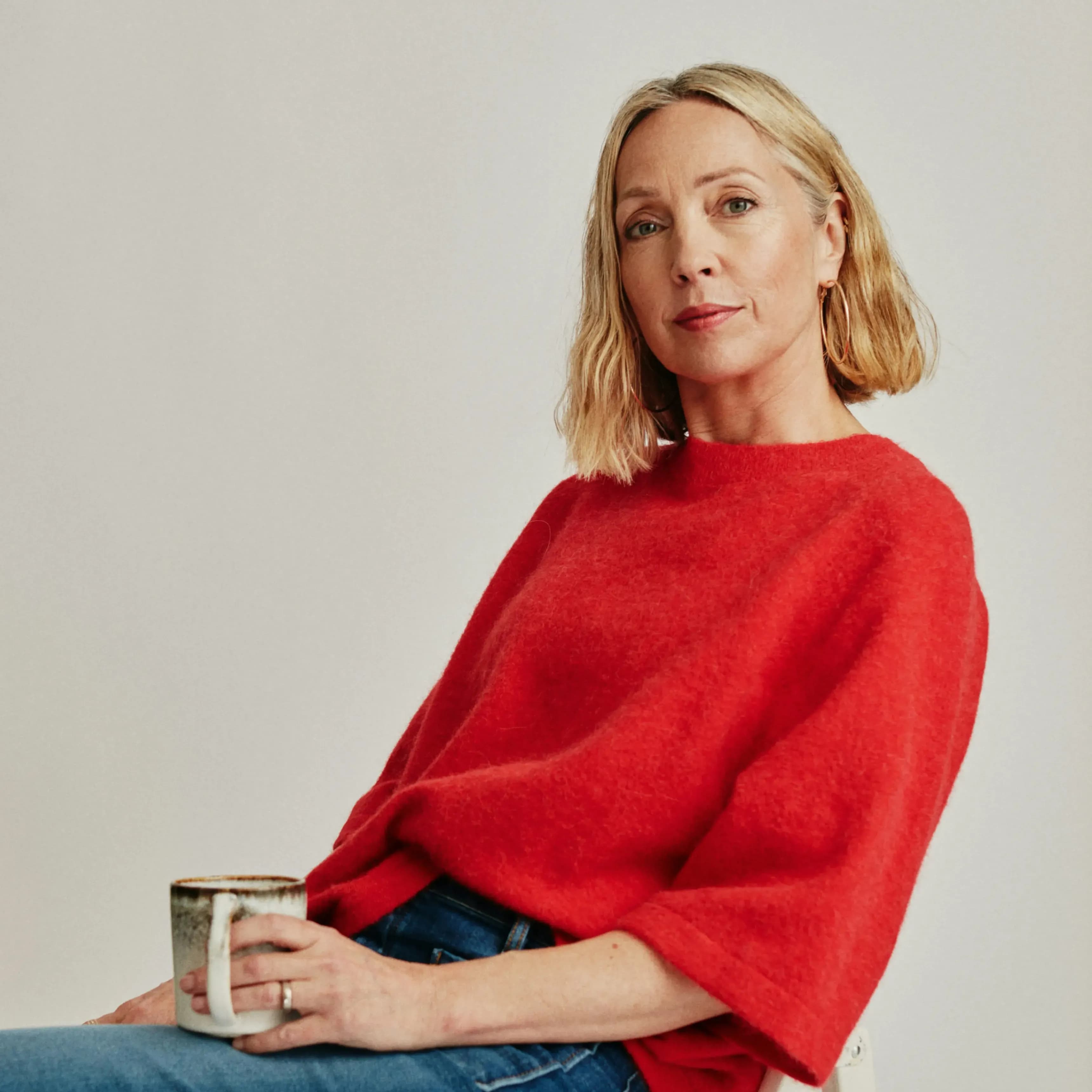 Person in a red sweater holding a mug, seated against a plain background.