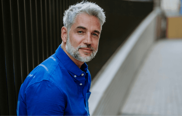 A vibrant looking older man in a blue shirt sitting outside.